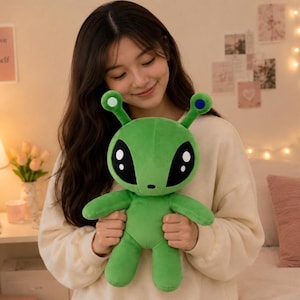 Peut inclure: Une peluche extraterrestre verte avec une grosse tête, deux antennes surmontées de cercles blanc et bleu, et de grands yeux noirs avec des reflets blancs. La créature a un petit nez, des bras et des jambes courts, en tissu doux.