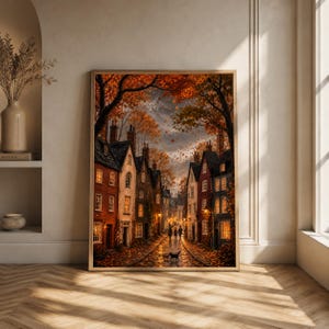 Pode incluir: Uma impressão de arte de parede vertical emoldurada retratando uma rua estreita de paralelepípedos ladeada por edifícios de tijolos de vários andares no outono. A cena apresenta janelas com luz quente, folhagem laranja e marrom.