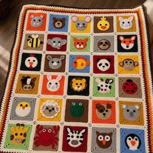 Può includere: Una coperta rettangolare all'uncinetto con una griglia di trenta quadrati colorati, ognuno dei quali mostra un diverso muso di animale all'uncinetto, tra cui un leone, una zebra, un granchio, una giraffa, una scimmia, un panda, un elefante e altri.