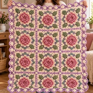 May include: A rectangular crochet blanket featuring a grid of twelve square motifs. Each square displays a three-dimensional pink flower center surrounded by cream petals and green leaves, all bordered by a scalloped purple and cream floral edge.