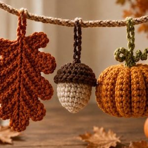 Peut inclure: Un ensemble de trois ornements crochetés suspendus à une corde tressée, comprenant une feuille de chêne rouille, un gland marron et crème, et une citrouille orange avec une tige verte. Chaque pièce possède une petite boucle en crochet.