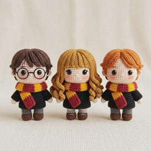 Pode incluir: Três bonecos amigurumi compostos por figuras de crochê com cabelo de lã preto, castanho e ruivo. Cada boneco veste um suéter preto, sapatos marrons e um cachecol listrado vermelho e amarelo. O boneco da esquerda tem óculos pretos redondos.