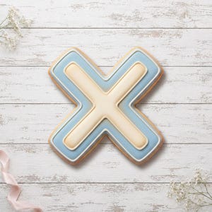 Peut inclure: Un biscuit en forme de lettre X décoré d'un glaçage lisse dans des tons bleu clair et crème. Le design présente un effet superposé en relief avec une section centrale en forme de croix couleur crème bordée d'un cadre bleu clair et blanc.