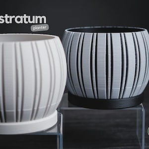 May include: Two round stratum planters with vertical ribbed textures. One planter is solid white with a matching base, and the other is light gray with a black interior and base. The text stratum planter appears in the upper left corner.