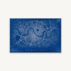 May include: A rectangular wall art print featuring a detailed white street map of a city on a deep blue background. The map displays a winding river flowing horizontally through the centre, with the word NASHVILLE printed in white at the bottom.