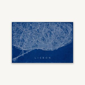 May include: A rectangular wall art print featuring a detailed white line map of Lisbon, Portugal, set against a deep blue background. The map displays intricate street grids and the 25 de Abril Bridge, with the word LISBON printed in white.