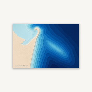 Pode incluir: Um mapa de arte em papel em camadas de Rehoboth Beach com uma massa de terra bege, uma grade de ruas e um oceano em vários tons de azul. A água transita do ciano claro perto da costa para o azul-marinho profundo, criando um efeito 3D.