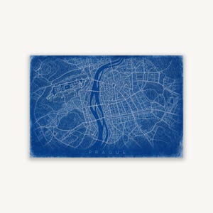 Puede incluir: Una impresión rectangular que muestra un mapa detallado de Praga estilo plano técnico con líneas blancas sobre un fondo azul intenso. El río Moldava fluye por el centro, con la cuadrícula de calles y el castillo de Praga claramente visibles.