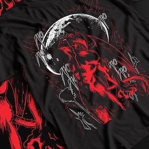 May include: A black short-sleeved t-shirt featuring a red and white graphic print of a winged creature with horns looking up toward a large white moon. The design includes stylized Japanese katakana characters surrounding the central figure.
