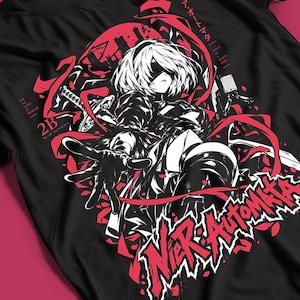 Könnte beinhalten: Ein schwarzes T-Shirt mit einem Grafikdruck der Figur 2B aus Nier: Automata. Das Design enthält rote und weiße Akzente, ein Schwert, fließende Bänder sowie den Text 2B, For the Glory of Mankind und Nier: Automata in stilisierten Schriftarten.
