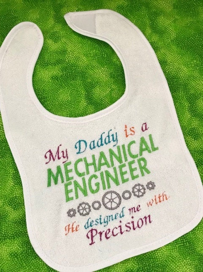 Puede incluir: Babero blanco con bordado de colores que dice "Mi pap&aacute; es un INGENIERO MEC&Aacute;NICO Me dise&ntilde;&oacute; con precisi&oacute;n" con s&iacute;mbolos de engranajes.