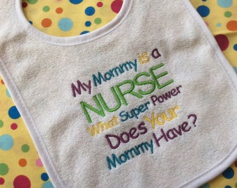 Op de afbeelding: Witte baby-slabbetje met de tekst "My Mommy is a NURSE What Super Power Does Your Mommy Have?" geborduurd in kleurrijk garen.