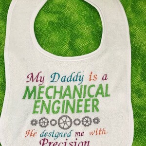 Puede incluir: Babero blanco con bordado de colores que dice "Mi pap&aacute; es un ingeniero mec&aacute;nico. Me dise&ntilde;&oacute; con precisi&oacute;n."