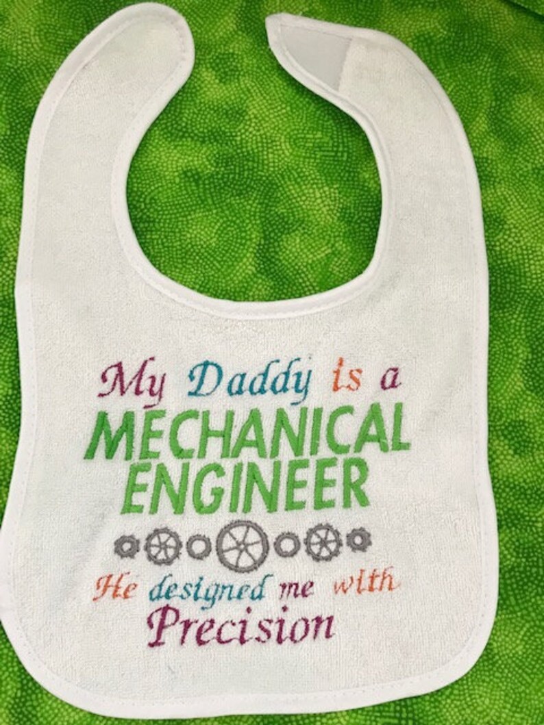 Puede incluir: Babero blanco con bordado de colores que dice "Mi pap&aacute; es un ingeniero mec&aacute;nico. Me dise&ntilde;&oacute; con precisi&oacute;n."
