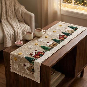 May include: A rectangular beige crochet table runner featuring a winter village scene with red and brown houses, green pine trees, yellow stars, and white snowflakes. The runner has a scalloped cream-coloured border and a textured, raised design.