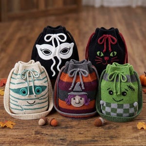 May include: Five crochet drawstring bags featuring Halloween-themed designs: a white mummy, a black mask, a black cat, a witch with a purple hat, and a green monster with a checkered base. Each bag has a matching drawstring closure.