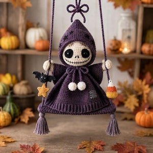 May include: A crocheted doll with a skull-like face and large black eyes, wearing a purple hooded cloak with star patterns. The doll sits on a purple swing with tassels, holding a small black bat, a yellow star, and a piece of candy corn.