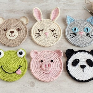 May include: Six round crochet coasters shaped like animal faces, including a brown bear, a cream rabbit with pink ears, a gray cat, a green frog with a tongue, a pink pig, and a black and white panda, all arranged in two rows of three.