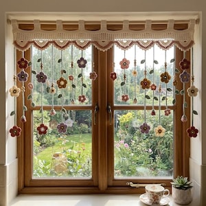 May include: A cream-coloured crochet valance featuring a scalloped edge and hanging vertical strands. Each strand is adorned with small, multi-coloured crocheted flowers in shades of red, purple, yellow, and pink, interspersed with green leaves.