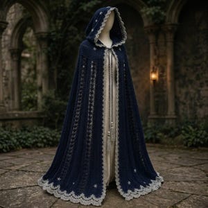 May include: A dark blue hooded cloak featuring a scalloped light gray lace trim along the edges. The cloak is decorated with small white star-shaped embroidery and includes a long braided cord tie with tassels at the front closure.