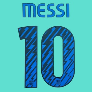 May include: A light turquoise sports jersey back featuring the name MESSI in bold blue lettering above the number 10. The number 10 is filled with a dark blue and light blue lightning bolt pattern and includes a small FC Barcelona club crest.