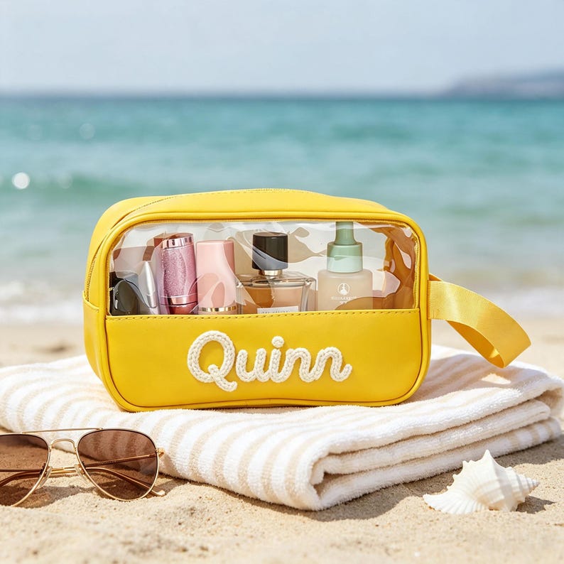 Puede incluir: Un neceser rectangular de color amarillo brillante con un panel frontal de pl&aacute;stico transparente y un asa lateral. El nombre Quinn est&aacute; bordado en letra blanca en la parte delantera. El neceser contiene varios frascos y envases cosm&eacute;ticos.