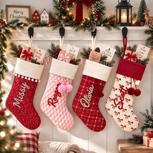 Op de afbeelding: Vier gewatteerde kerstsokken hangen aan zwarte haken. De eerste is rood met witte pompons en de naam Missy. De tweede is roze geruit met de naam Reagan. De derde is rood geruit met de naam Olivia. De vierde is wit met rode strikken en de naam Scott.