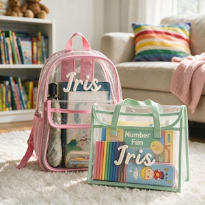 Op de afbeelding: Een doorzichtige rugzak met roze randen en een doorzichtige tas met lichtgroene randen, beide gepersonaliseerd met de naam Iris in witte schrijfletters. De rugzak bevat boeken en een paraplu, terwijl de tas een boek genaamd Number Fun en potloden bevat.
