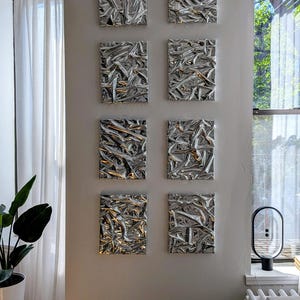 Op de afbeelding: Een set van acht rechthoekige wandkunststukken gerangschikt in twee verticale kolommen. Elk stuk heeft een sterk reflecterend, metallic zilveren oppervlak met een diep gekreukelde, verfrommelde textuur die licht en schaduw vangt.