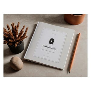 Puede incluir: Un libro de color gris claro con una etiqueta blanca en la portada que muestra un icono de arco negro y el texto SEVEN NIGHTS. El libro está colocado junto a un lápiz marrón, una maceta negra pequeña con plantas secas y una piedra lisa.