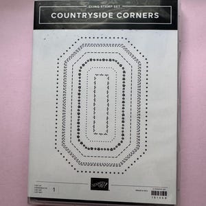 May include: A rectangular clear plastic case containing a cling stamp set titled Countryside Corners. The insert displays four nested octagonal frame designs in black ink, featuring various dotted, dashed, and floral patterns on a white background.
