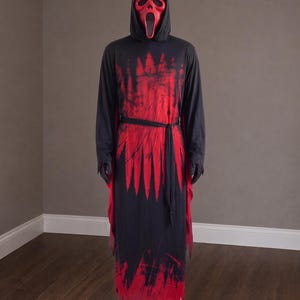 May include: A full-length black hooded robe featuring a red splatter pattern across the chest and hem, paired with a red mask that has two small horns on the forehead and a wide, open-mouthed expression, worn on a mannequin figure.