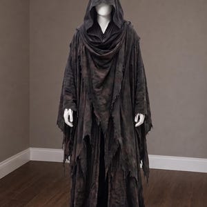 May include: A dark charcoal gray hooded cloak featuring a distressed, tattered hemline and layered fabric construction. The garment includes a deep cowl hood and long, flowing sleeves with frayed edges, draped over a plain black base layer.