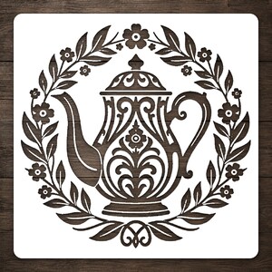 May include: A square stencil featuring a central dark brown teapot design with intricate scrollwork and filigree details. The teapot is surrounded by a circular wreath composed of dark brown leaves and small five-petaled flowers on a white background.