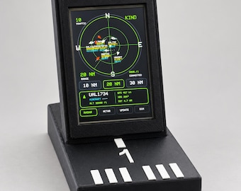 May include: A black desktop radar display unit featuring a vertical screen with a circular green navigation interface showing traffic, altitude, and speed data. The base includes white runway-style markings and a prominent number one symbol.