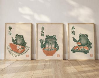May include: Three framed art prints featuring green frogs. The left print shows a frog with a bento box and the text 弁当. The center print shows a frog eating noodles from a bowl with the text 清風麺. The right print shows a frog with sushi and the text 寿司.