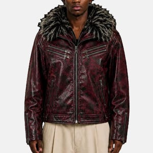 May include: A dark red and black mottled jacket featuring a large, thick faux fur collar in black and white. The jacket includes a central zipper closure, two horizontal zippered chest pockets, two lower zippered pockets, and zippered sleeve cuffs.