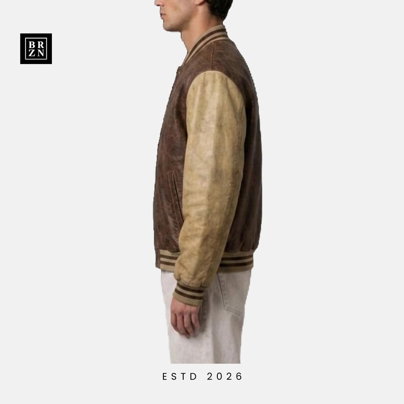 May include: A varsity-style jacket featuring a dark brown leather body and contrasting light tan leather sleeves. The garment includes a ribbed collar, cuffs, and hem with brown stripes. A black square logo with the text BR ZN is visible.