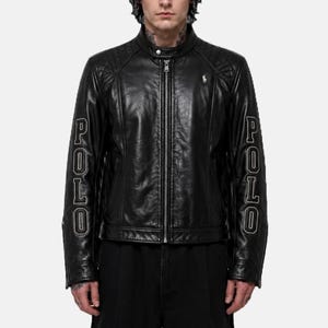 May include: A black leather jacket featuring a full-length front zipper, a snap-button collar, and quilted shoulder panels. The word POLO is embroidered in white on both sleeves, and a small white embroidered horse logo is on the chest.