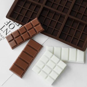 May include: A dark brown silicone mold with a grid pattern, accompanied by three rectangular bars. One bar is light brown with small squares, another is medium brown with larger rectangular segments, and the third is a white square with a grid pattern.
