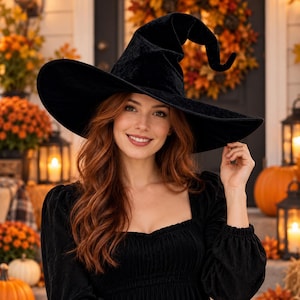 May include: A black velvet witch hat with a wide, structured brim and a tall, pointed, slightly curved crown. The hat features a soft, textured fabric finish and is designed with a classic conical shape that tapers to a distinct point.
