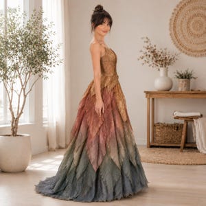 May include: A floor-length gown featuring a bodice and skirt constructed from layered, leaf-shaped fabric panels. The dress displays a gradient color transition, starting with golden-brown at the top, shifting to muted rose, and ending in deep forest green at the hem.