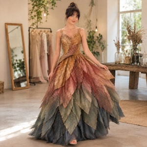 May include: A floor-length gown featuring a bodice and skirt constructed from layered, leaf-shaped fabric panels in a gradient of autumn colors, transitioning from golden yellow and burnt orange at the top to deep forest green and charcoal gray at the hem.