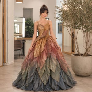 May include: A floor-length gown featuring a bodice and skirt constructed from layered, leaf-shaped fabric panels. The color palette transitions from golden yellow at the top, through shades of rust and muted red, to dark charcoal gray at the hem.