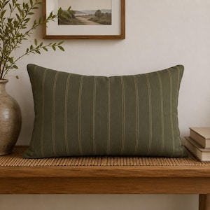 May include: A rectangular throw pillow in a deep olive green fabric featuring thin, vertical mustard yellow pinstripes. The pillow has a structured, filled appearance with clean, straight edges and a consistent, woven texture across the entire surface.