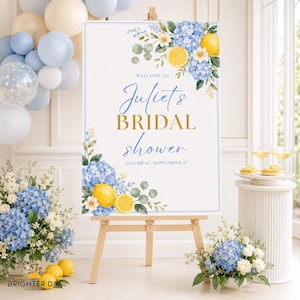 May include: A rectangular bridal shower welcome sign on a wooden easel featuring watercolor illustrations of blue hydrangeas, yellow lemons, and green leaves. The text reads: WELCOME TO Juliet's BRIDAL shower SATURDAY, SEPTEMBER 27.