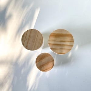 May include: Three round wooden lids with a natural wood grain finish. The lids are different sizes and are arranged in a triangular pattern on a white surface.