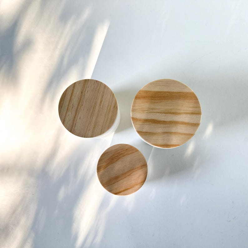 May include: Three round wooden lids with a natural wood grain finish. The lids are different sizes and are arranged in a triangular pattern on a white surface.