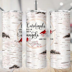 May include: A white tumbler featuring a birch bark pattern and the text "Cardinals Appear When Angels Are Near." The design includes red cardinals on branches with red berries. A silver straw is inserted in the lid.