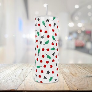 Puede incluir: Un vaso blanco con un patr&oacute;n de bayas de acebo rojas y verdes y estrellas.